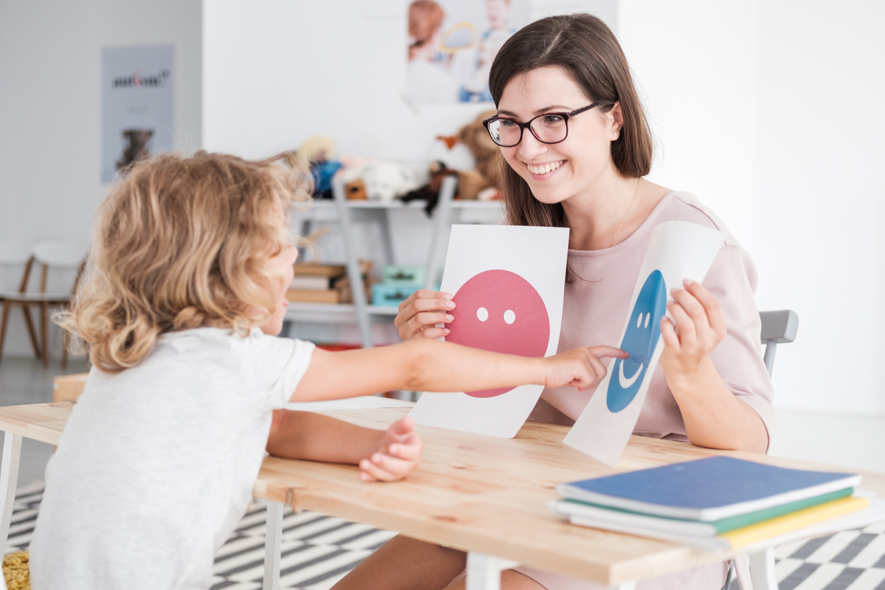 Smiling counselor holding pictures during meeting with young patient with autism School Counselor and Boy